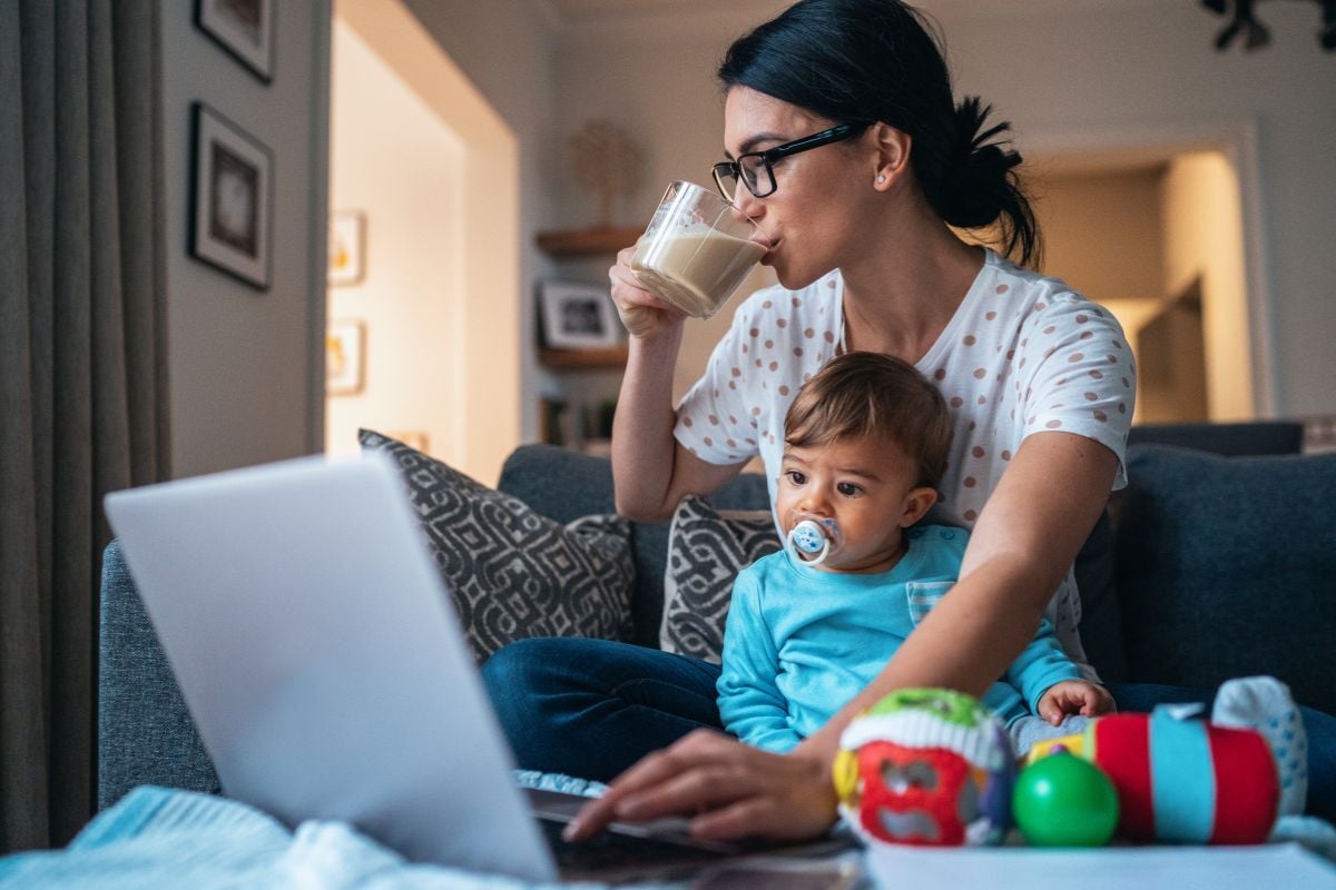 Mother sitting with her child while using a laptop at home